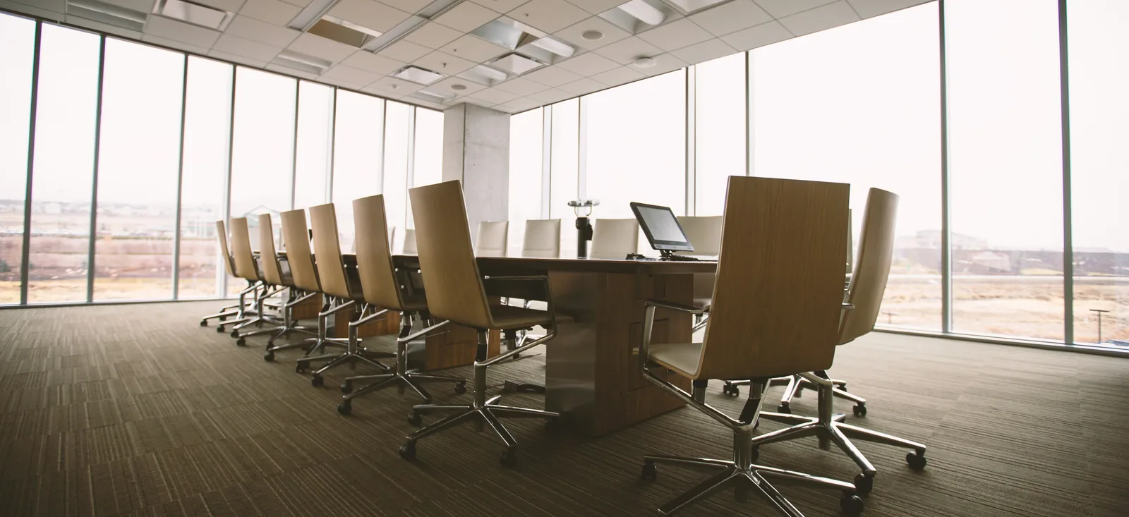 A long wooden conference table with chairs in a bright office with floor-to-ceiling windows